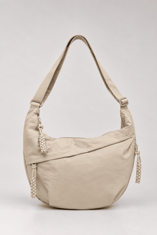 Bolso bandolera de nylon con forma de media luna en color beige, de la marca Vera Serrat, con detalles elegantes y funcionales.